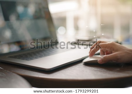 Female hand with computer mouse on table, hand using mouse and laptop computer in modern office with virtual screen interface icons diagram as concept.