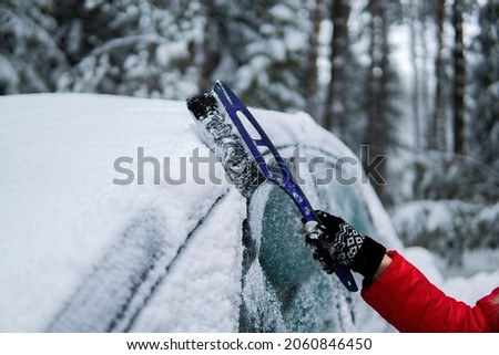 female hand counting snow with a duster on the car on the background of a snowy forest.