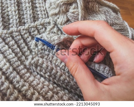 Female hand and crochet hook with gray woolen winter scarf collar, crocheting antistress therapy. English rib stitch with a single crochet, hygge concept