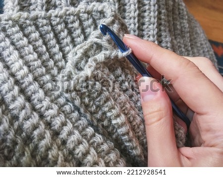 Female hand with crochet hook making gray woolen winter scarf collar, crocheting antistress therapy, hygge concept. English rib stitch with a single crochet