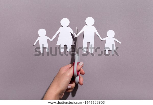 Female hand cutting Paper family\
chain on gray background, divorce or family problems\
concept