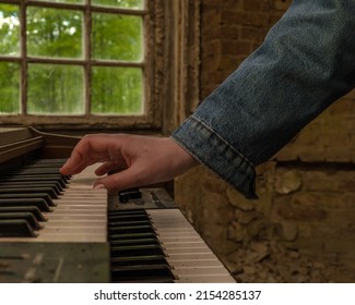 Female hand in a denim jacket plays an old dusty synthesizer in a room with destroyed walls