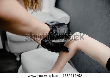 Female hand depilation.Beauty concept - sugar paste or wax honey for hair removing with black gloves hands of cosmetologist in spa salon