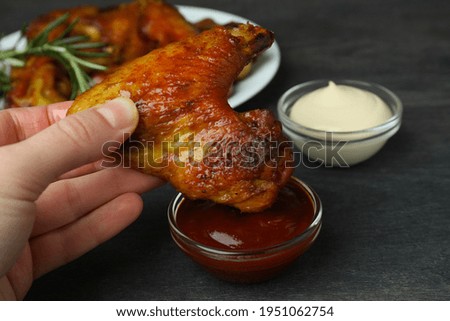 Female hand dipping baked chicken wing into sauce, close up