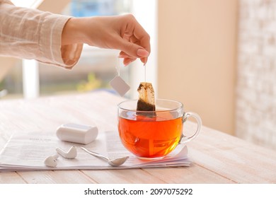 Female hand dipping tea bag in hot water at table in cafe