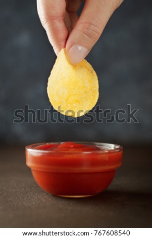 Female hand dips chip into tomato sauce or ketchup. Concept of unhealthy junk food.