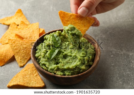 Female hand dips chips slice in guacamole, close up