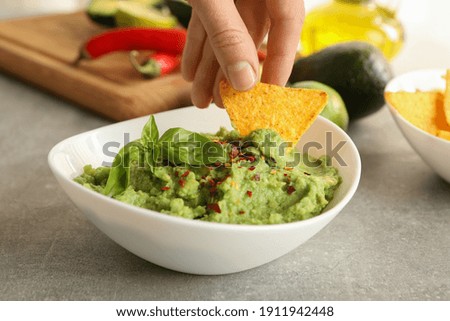 Female hand dips chips slice in guacamole, close up