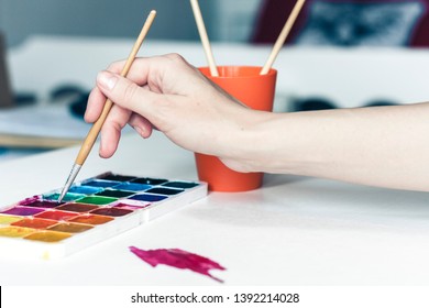 female hand draws with a brush and watercolor paint on a sheet of paper on white wooden table with copy space for text - Powered by Shutterstock