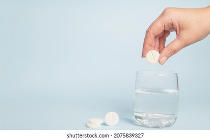 Female hand dropping pill vitamin C into glass of water on light blue background