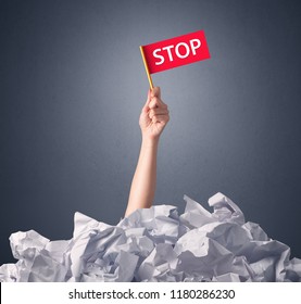 Female Hand Emerging From Crumpled Paper Pile Holding A Red Flag With Stop Written On It 