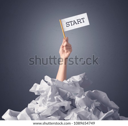 Female hand emerging from crumpled paper pile holding a white flag with start written on it