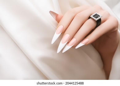 Female hand with french stiletto nail design. Long pink nail polish manicure. Woman hand on white fabric background.