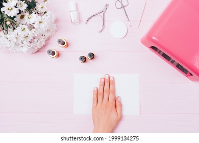 Female Hand With Gel Manicure Among Tools And Cosmetic Products Next To UV Lamp, Flat Lay On Pink Table.