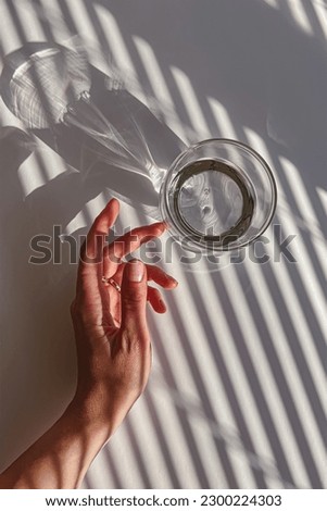 Female hand gently touching a glass of clear water, view from the top, abstract shadows, morning light 商業照片 © 