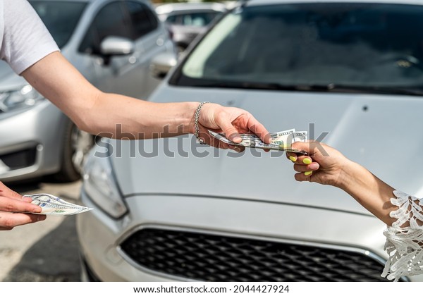 female hand gives dollar to a salesman when\
buying a new modern car, sale\
concept