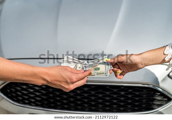 female hand gives dollar to a salesman when\
buying a new modern car, sale\
concept