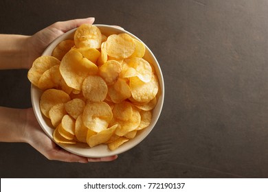 Female hand giving crispy potato chips bowl. Top view with copy space.