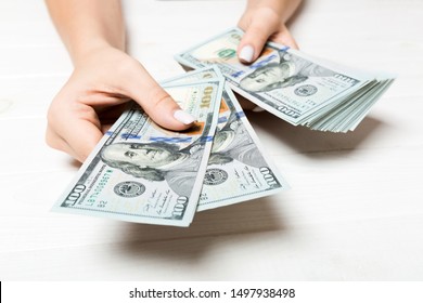 Female hand giving one hundred dollar banknotes on wooden background. Perspective view of wealth concept.
