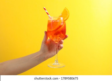 Female hand with glass of aperol spritz cocktail on yellow background
