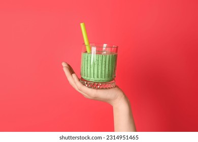 Female hand with glass of green smoothie on red background - Shutterstock ID 2314951465