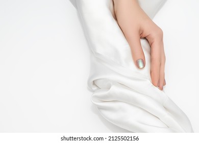 Female Hand With Glitter Pearlescent Nail Design. Glitter Pearlescent Nail Polish Manicure. Female Model Hand With White Fabric On White Background. Copy Space