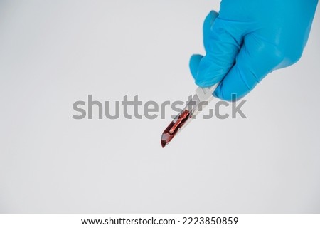 Female hand in a glove with a bloody scalpel on a white background. Copyspace. 