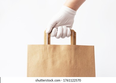 Female Hand In A Glove Holds Brown Cardboard Bag On White Background, Food Delivery Concept.