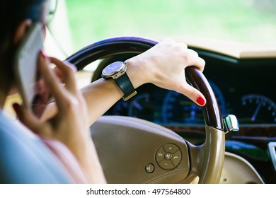 Female hand with gold black watch holding leather steering wheel in car