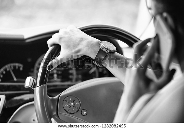 Female hand with gold black watch holding leather\
steering wheel in car
