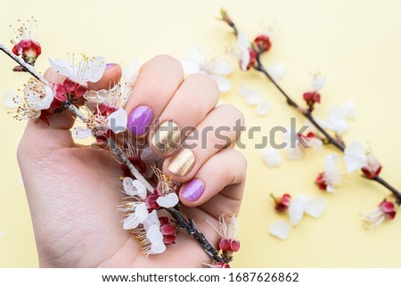 Female hand with gold and purple nail design holding blossom cherry branch
