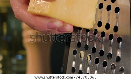 Female hand grating cheese against a dark background. Close-up shot