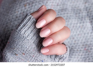 Female hand in gray knitted sweater with beautiful natural manicure - pink nude nails. Nail care concept
