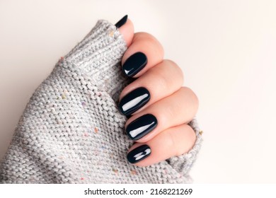 Female hand in gray knitted sweater with beautiful manicure - dark black nails. Nail care concept
