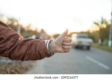 Female hand and hitchhiking sign on road, traveling by autostop in the city. Woman try stop car thumb up. Adventure and tourism.