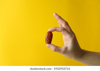 Female Hand Hold Date Fruit On Yellow Background