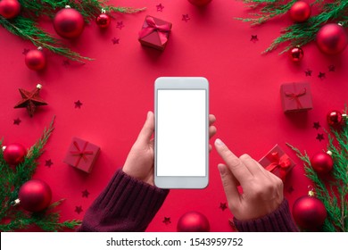 Female hand hold phone on merry christmas red background, girl customer shopper using online mobile shopping app choosing holiday gifts with mobile payments on mock up white screen, close up top view - Powered by Shutterstock