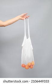 Female hand hold white mesh bag with fruit.Modern reusable shopping, zero waste concept.