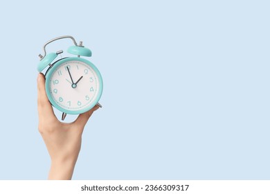 Female hand holding alarm clock on blue background - Powered by Shutterstock