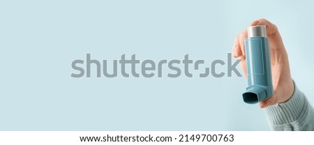 Female hand holding asthma inhaler on light blue background with space for text
