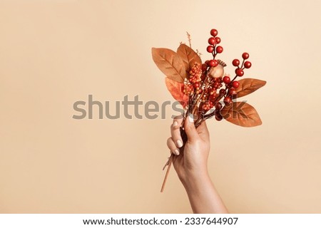 female hand holding autumn bouquet with red leaves and berries, beige background with copy space