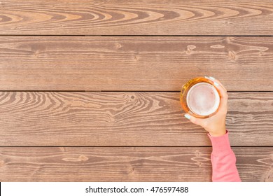 Female hand holding beer glass over wooden table