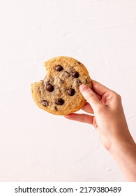 Female Hand Holding Bitten An American Chocolate Chip Cookie In The Air In Front Of The White Background, Homemade