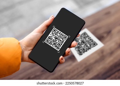 female hand holding black mobile phone with qr code on the screen. scanning the qr code