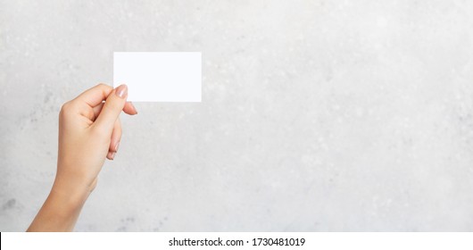 Female Hand Holding A Blank Business Card, Cutaway On Gray Concrete Background With Copy Space. Branding Mockup Template. Mockup