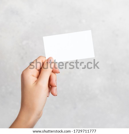 Female hand holding a blank business card, cutaway on gray concrete background with copy space. Mockup