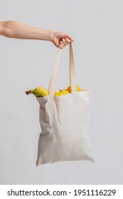 Female Hand Holding Blank Eco Tote Bag With Organic Fruits And Vegetables Over Light Studio Background, Unrecognizable Lady Using Reusable Canvas Bag For Grocery Shopping, Closep Shot