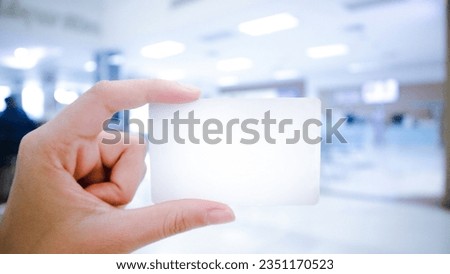 Female hand holding blank hospital card, business or discount card Mockup of hospital membership card, insurance card. Over the reception room of a hospital or clinic hospital, blurred in the bac