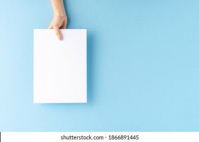 Female Hand Holding Blank White Paper Sheet On Blue Background. Mock Up