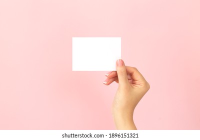Female hand holding blank white business card, discount or flyer on pink background with copy space. Template for your design